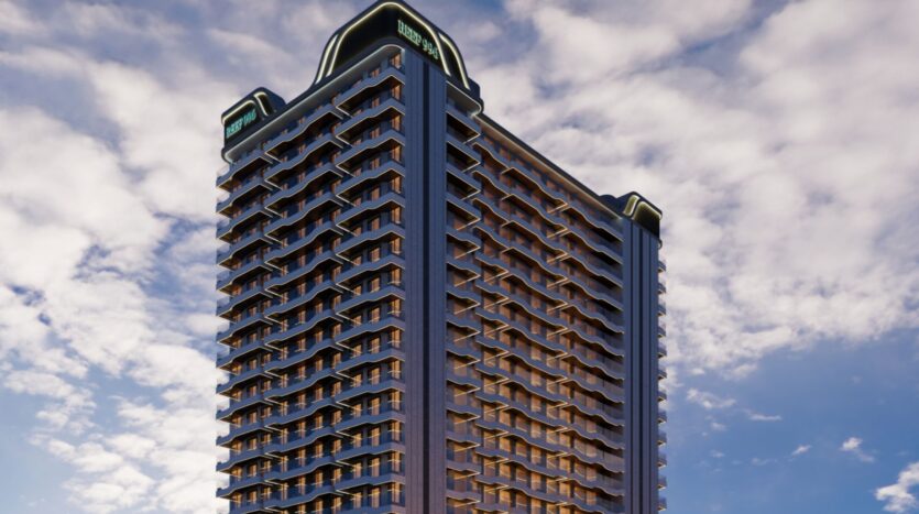 Reef 996, un grand immeuble moderne, présente de nombreux balcons et des motifs géométriques dans un ciel partiellement nuageux. La lumière chaude du soleil met en valeur la structure, tandis que la signalisation de Reef 996 est visible dans les coins supérieurs du bâtiment.