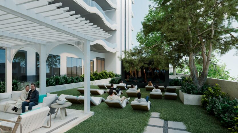 Des personnes se détendent sur des chaises longues et des canapés face à un grand écran extérieur dans un jardin moderne avec des arbres, de la verdure et une pergola blanche à côté du bâtiment contemporain Reef 996.