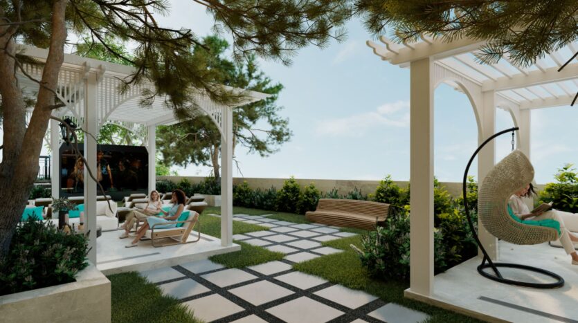 Salon extérieur avec des personnes se relaxant sur des canapés sous des pergolas blanches, entourées de verdure et d'arbres. Un fauteuil suspendu Reef 996 se trouve à droite, avec un banc en bois à l'arrière-plan, sur une terrasse en pierre et en gazon à motifs.