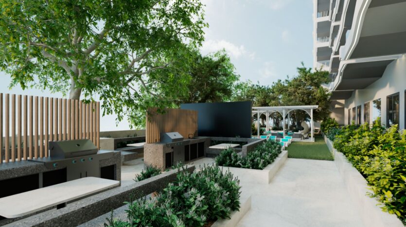 Terrasse moderne avec grilles de barbecue Reef 996, comptoirs en pierre, bancs, plantes vertes luxuriantes, pelouse et un coin salon ombragé sous des pergolas blanches à côté d'un bâtiment contemporain lors d'une journée ensoleillée.