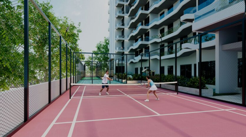 Deux personnes jouent au padel sur un court Reef 996 rose vif entouré d'une clôture, avec un immeuble d'habitation moderne, des arbres et de la verdure en arrière-plan.