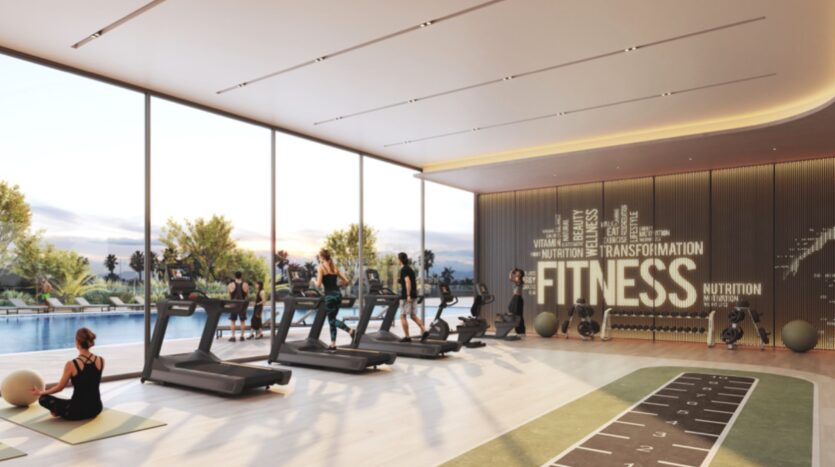 Une salle de sport moderne dans les résidences Rotana avec de grandes fenêtres donnant sur une piscine, avec des tapis de course, des personnes faisant de l'exercice, des tapis de yoga, des équipements de fitness et un mur avec des mots motivants comme "FITNESS" et "TRANSFORMATION".