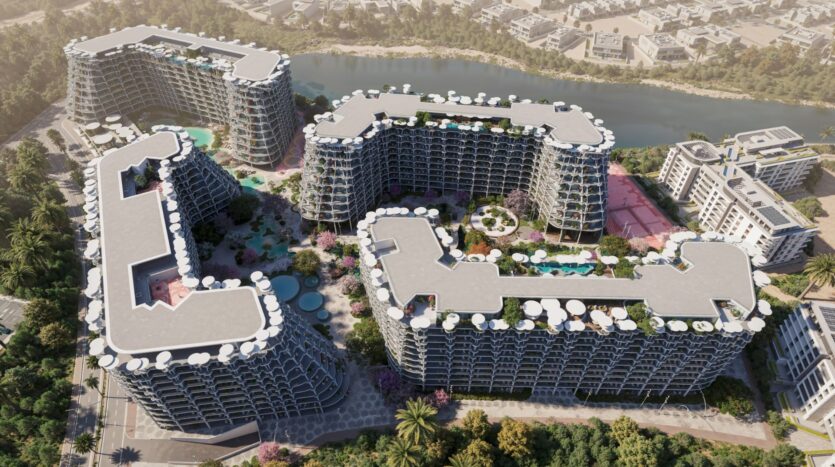 Vue aérienne de Sakura Gardens, un complexe d'appartements moderne, composé de plusieurs bâtiments, avec des balcons circulaires, des piscines environnantes et des jardins près d'une rivière et d'une végétation luxuriante, avec d'autres bâtiments et des routes en arrière-plan.