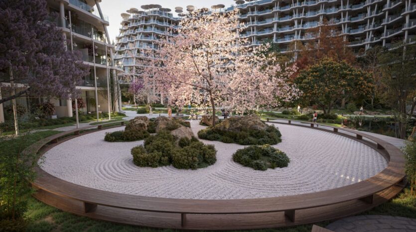 Un jardin zen rond de Sakura Gardens se compose de gravier blanc ratissé, de gros rochers et d'un cerisier en fleurs dans une cour moderne entourée de bâtiments incurvés et d'une verdure luxuriante.