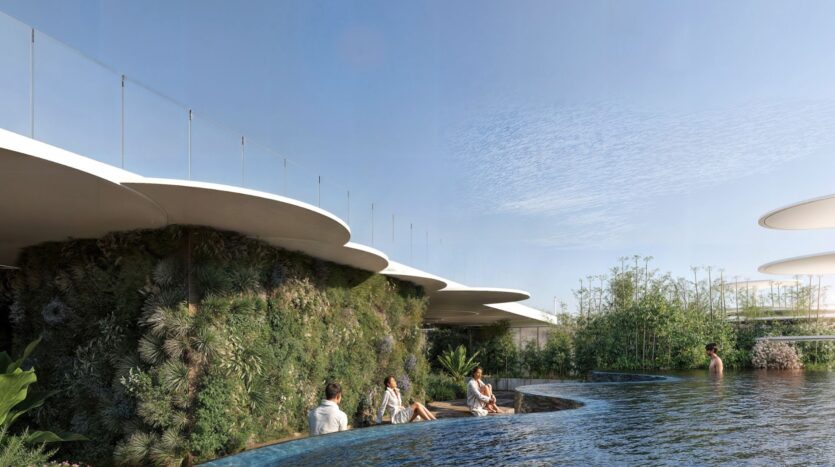Des personnes se détendent au bord d'une piscine à Sakura Gardens, entourée d'une végétation luxuriante et d'une architecture moderne et incurvée. Des barrières de verre surmontant des murs verts et des plantes abondantes créent un environnement extérieur tranquille et naturel sous un ciel bleu limpide.