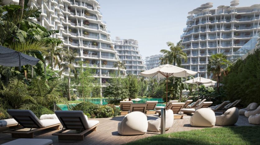 Des chaises longues et des parasols entourent une piscine au milieu d'une végétation luxuriante à Sakura Gardens, avec en arrière-plan des gratte-ciel modernes et incurvés sous un ciel clair.