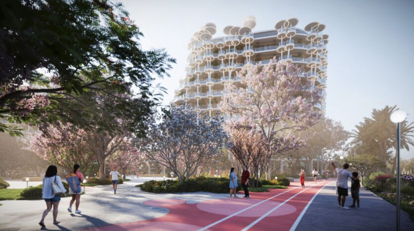 Des personnes marchent sur un chemin coloré entouré d'arbres en fleurs dans les jardins de Sakura, devant un bâtiment moderne aux balcons circulaires, sous un ciel radieux.