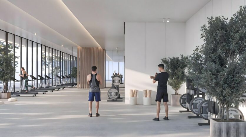 Une salle de sport moderne et spacieuse dans Sakura Gardens avec de grandes fenêtres, plusieurs tapis de course sur la gauche, des appareils d'haltérophilie, deux personnes faisant de l'exercice et des plantes en pot dans tout l'espace propre et minimaliste.
