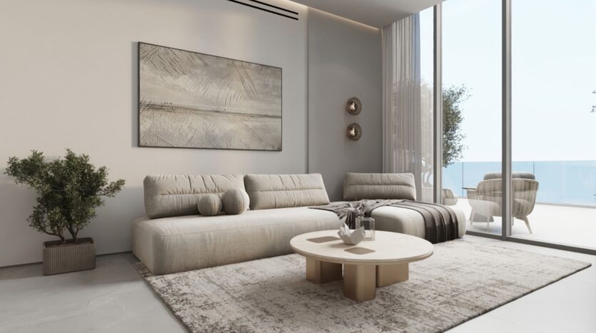 Un salon moderne avec un canapé sectionnel beige, une table basse ronde, des œuvres d'art murales abstraites et un décor neutre, inspiré des jardins de Sakura. De grandes portes vitrées s'ouvrent sur un balcon où l'on peut s'asseoir en plein air et qui offre une vue imprenable sur l'océan.