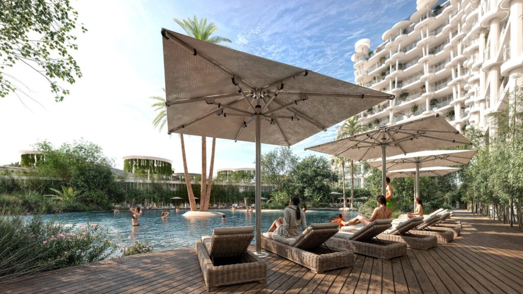 Des personnes se détendent sur des chaises longues en osier sous de grands parasols au bord d'une piscine à Sakura Gardens, entourée de verdure et de bâtiments blancs modernes avec des balcons. Quelques personnes nagent dans la piscine en cette journée ensoleillée.