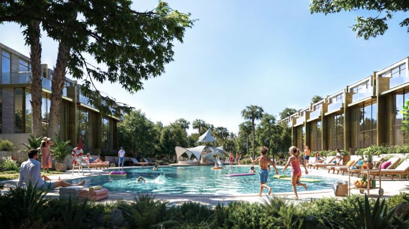 Les enfants jouent près d'une piscine extérieure moderne à Tilal by Binghatti, entourée de chaises longues, d'adultes en train de se détendre et de bâtiments contemporains avec de la verdure et des palmiers sous un ciel bleu clair.