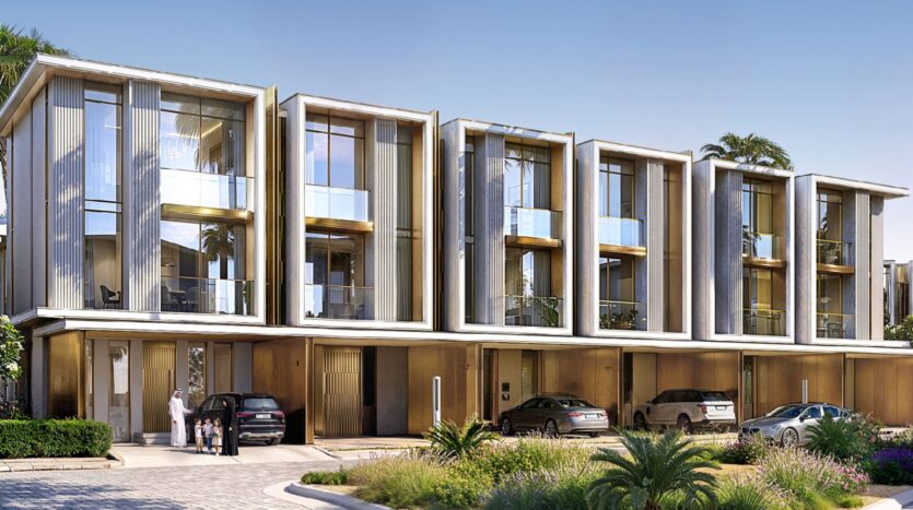 Rangée moderne de maisons de ville de trois étages à Tilal by Binghatti, avec de grandes baies vitrées et des balcons, avec des voitures garées devant et des espaces verts aménagés. Une famille se tient près de l'entrée d'une maison sous un ciel bleu clair.