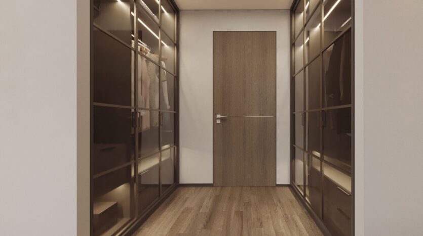 Un dressing moderne avec des armoires vitrées des deux côtés, avec des vêtements et des étagères, et une porte en bois à l'extrémité. L'espace est doté d'un éclairage chaleureux, d'un plancher en bois et d'un design élégant inspiré de Tivanno by AYS.