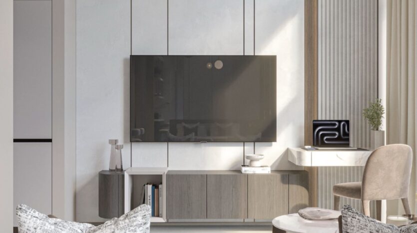 Salon moderne comprenant un téléviseur mural à écran plat, un meuble élégant Tresora by Wadan, des objets de décoration, une petite table ronde, un coussin à motifs et un bureau avec un ordinateur portable près de hautes fenêtres avec des rideaux.