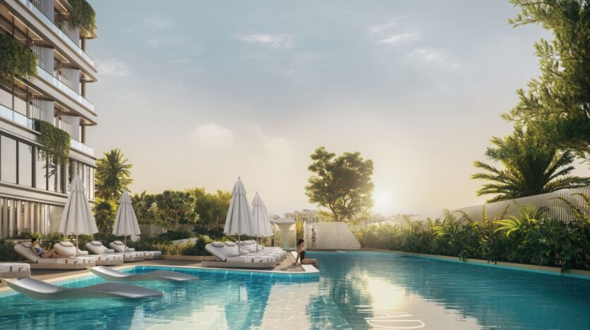 Une piscine extérieure sereine au lever du soleil à Tresora by Wadan, entourée d'une végétation luxuriante et de bâtiments modernes. Des chaises longues et des parasols blancs bordent la piscine, avec une personne assise paisiblement au bord de l'eau.