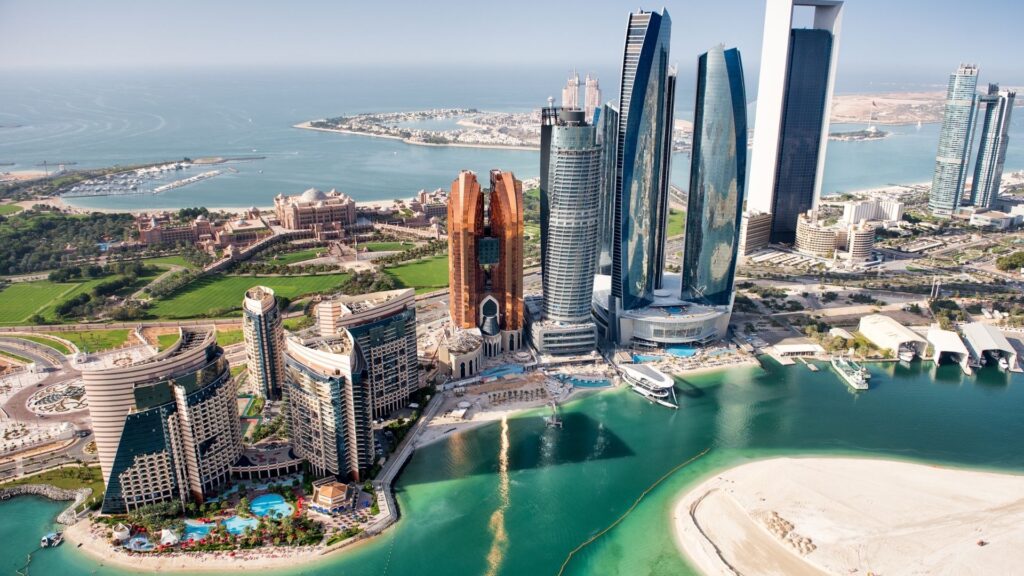 Vue aérienne de la ligne d'horizon d'Abu Dhabi avec ses gratte-ciel modernes, ses hôtels, sa plage, son eau turquoise et ses espaces verts - on peut apercevoir les avantages et inconvénients de l'immobilier à Abu Dhabi sur fond de golfe Persique qui s'étend au loin.