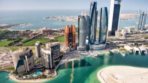 Vue aérienne de la ligne d'horizon d'Abu Dhabi avec ses gratte-ciel modernes, ses hôtels, sa plage, son eau turquoise et ses espaces verts - on peut apercevoir les avantages et inconvénients de l'immobilier à Abu Dhabi sur fond de golfe Persique qui s'étend au loin.