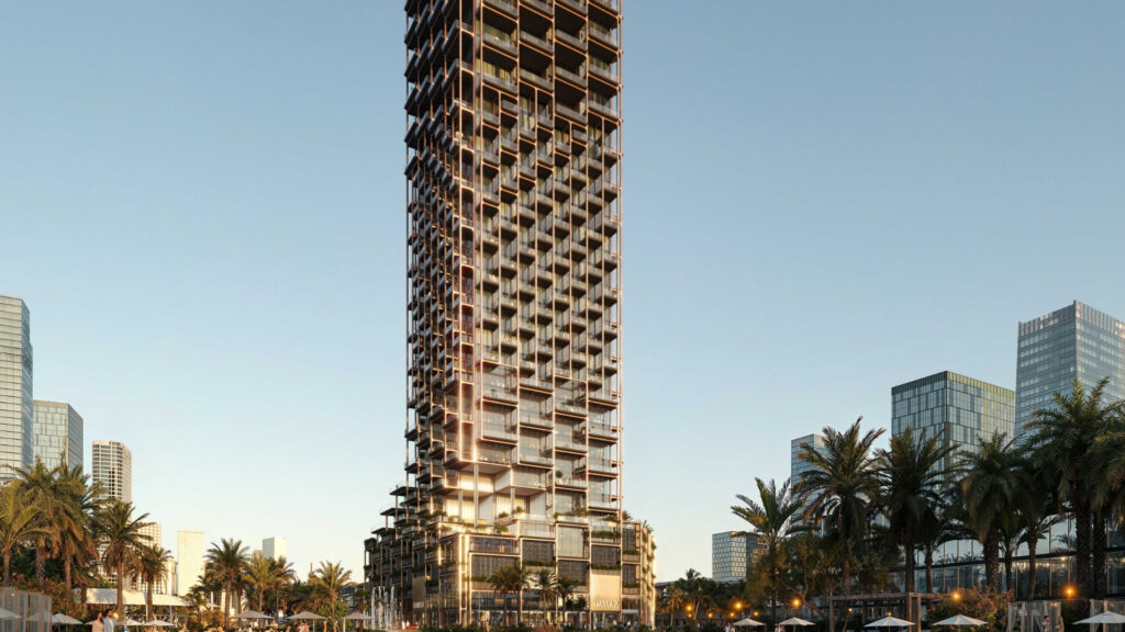 Un grand gratte-ciel moderne à la façade irrégulière et quadrillée se dresse au milieu des palmiers et d'autres gratte-ciel au coucher du soleil, alors que les lumières commencent à éclairer l'un des quartiers de Dubaï prisés par les investisseurs français dans l'immobilier à Dubaï.
