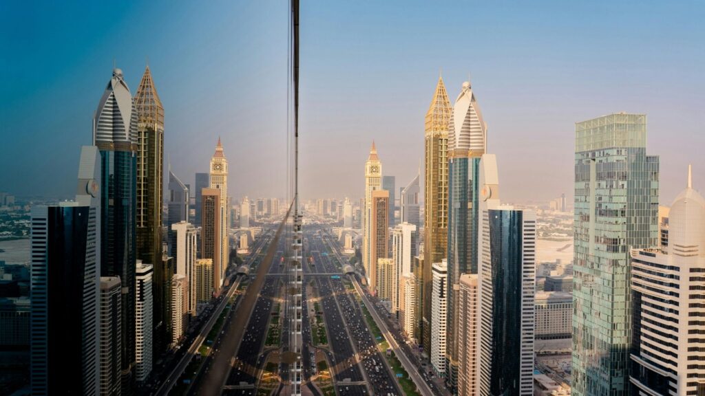 La vue d'une ville avec de hauts gratte-ciel et une route très fréquentée, qui se reflète parfaitement dans la façade en verre d'un bâtiment, évoque l'énergie dynamique du Marché immobilier de Dubaï sous un ciel dégagé.