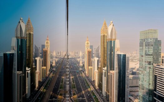 La vue d'une ville avec de hauts gratte-ciel et une route très fréquentée, qui se reflète parfaitement dans la façade en verre d'un bâtiment, évoque l'énergie dynamique du Marché immobilier de Dubaï sous un ciel dégagé.