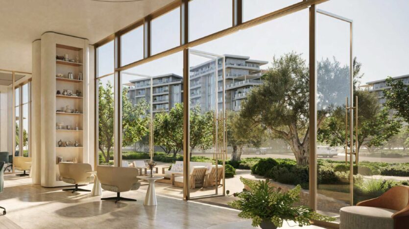 Salon moderne avec des chaises et des tables de couleur claire, des murs en verre allant du sol au plafond et des vues sur les jardins paysagers et les arbres à l'extérieur. Les immeubles d'appartements d'Arancia Yards by Beyond sont visibles à l'arrière-plan à travers les grandes fenêtres.
