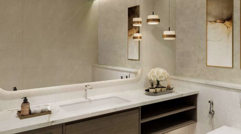 Salle de bains moderne avec un comptoir en marbre, un lavabo, un distributeur de savon, des serviettes et un plateau avec des fleurs décoratives. Les lampes suspendues et l'art mural abstrait au-dessus du meuble-lavabo créent un look luxueux inspiré par Arancia Yards by Beyond. Un grand miroir reflète l'élégance du décor.
