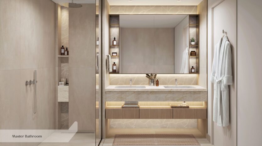 La salle de bains principale moderne de l'Everly Place by Ellington comprend un meuble-lavabo à double vasque, un grand miroir, une douche à l'italienne, des murs carrelés de couleur beige, des étagères encastrées avec des articles de toilette et des peignoirs près de la porte. Un éclairage chaleureux crée une atmosphère douillette.