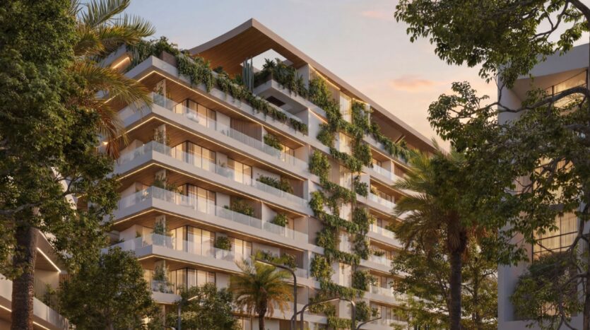 Lunaya Terraces est un immeuble d'appartements moderne doté de grands balcons, de végétation luxuriante à chaque étage et d'un toit en bois, entouré de grands arbres au coucher du soleil.