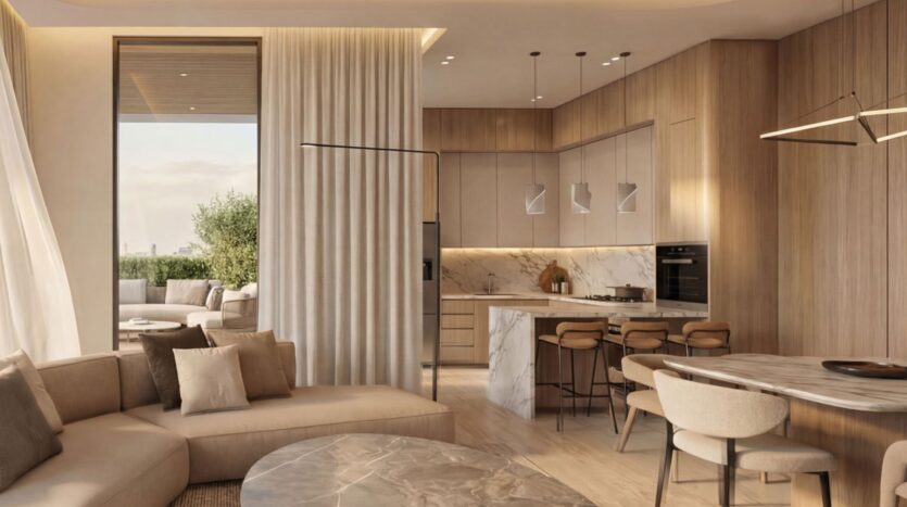 Salon et cuisine modernes en espace ouvert à Lunaya Terraces, avec des finitions en bois clair, des touches de marbre, un canapé modulable beige, une table basse ronde, un coin repas et une vue depuis le balcon sur le coin salon extérieur et la verdure à travers de grandes baies vitrées.