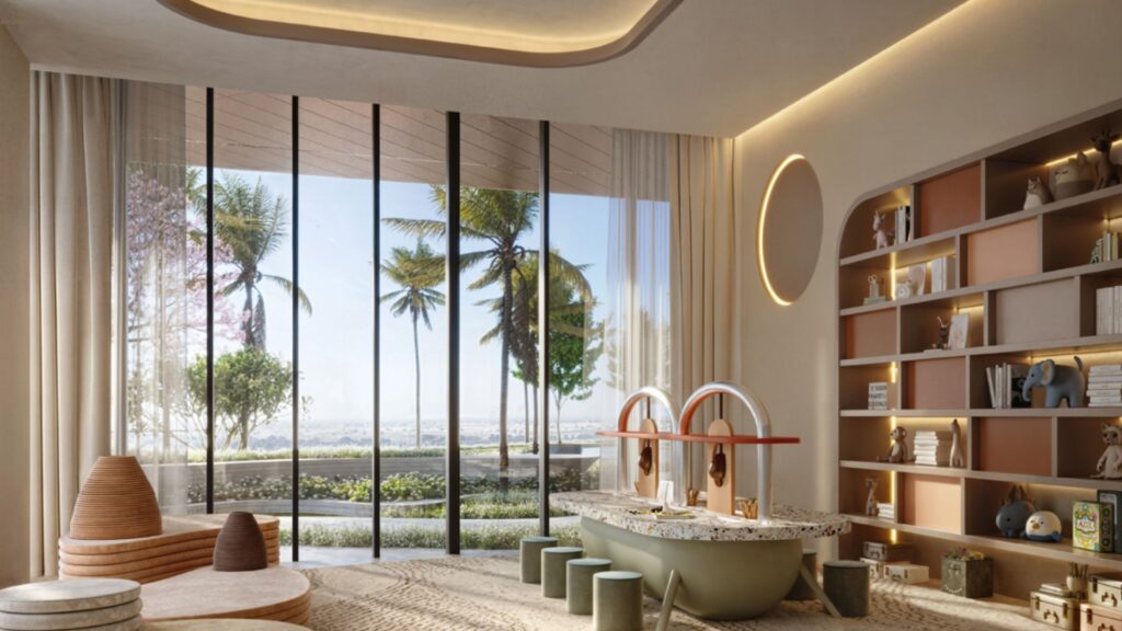 Une salle de jeux moderne au Mövenpick Residences, dotée d'une grande baie vitrée donnant sur des palmiers et de la verdure, avec des sièges bas, une table de jeux garnie de jouets, une bibliothèque encastrée contenant divers objets, et un éclairage naturel et tamisé.