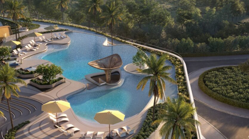 Vue aérienne de la luxueuse piscine extérieure des Mövenpick Residences, avec ses bords incurvés, ses transats, ses parasols à rayures jaunes, ses palmiers et sa structure centrale unique, le tout entouré de verdure et d'une route sinueuse.