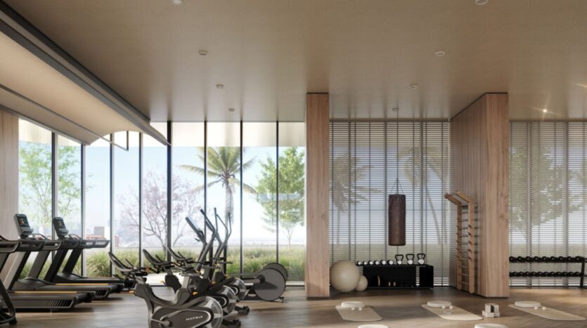 Salle de sport moderne au Mövenpick Residences, équipée de tapis de course, de vélos d'appartement, d'haltères, de tapis de yoga et d'appareils de fitness. De grandes baies vitrées donnent sur les palmiers et la verdure à l'extérieur, inondant de lumière naturelle cette salle spacieuse au style minimaliste.