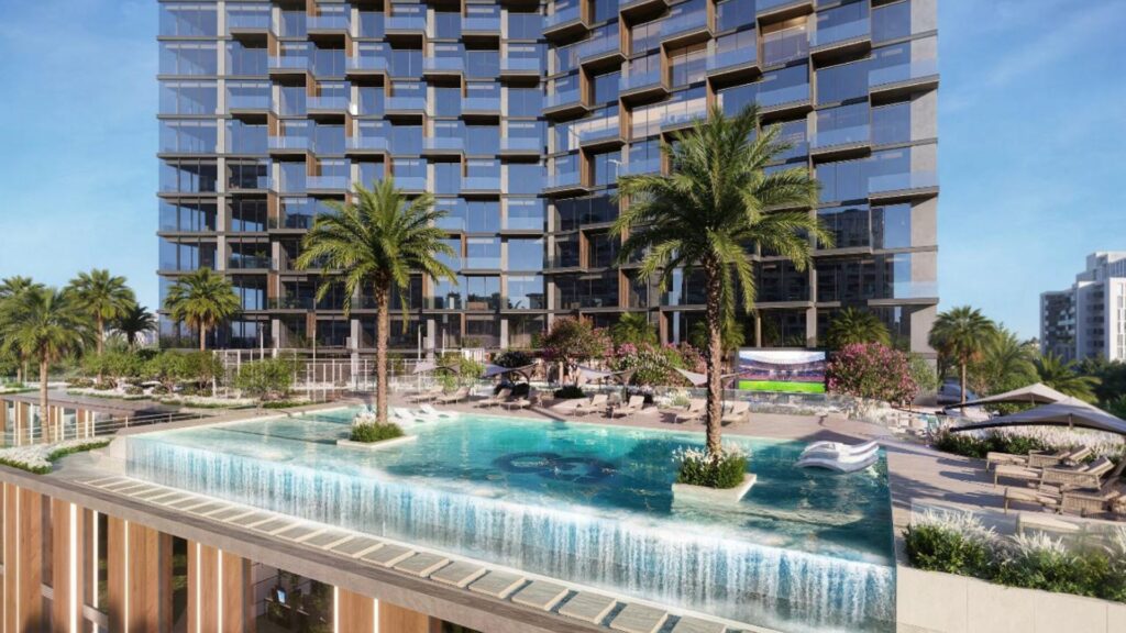 Un bâtiment Winslow moderne avec des balcons en verre surplombe une piscine à débordement surélevée avec un bord en cascade, entourée de palmiers, de chaises longues et de sièges en plein air par temps ensoleillé.