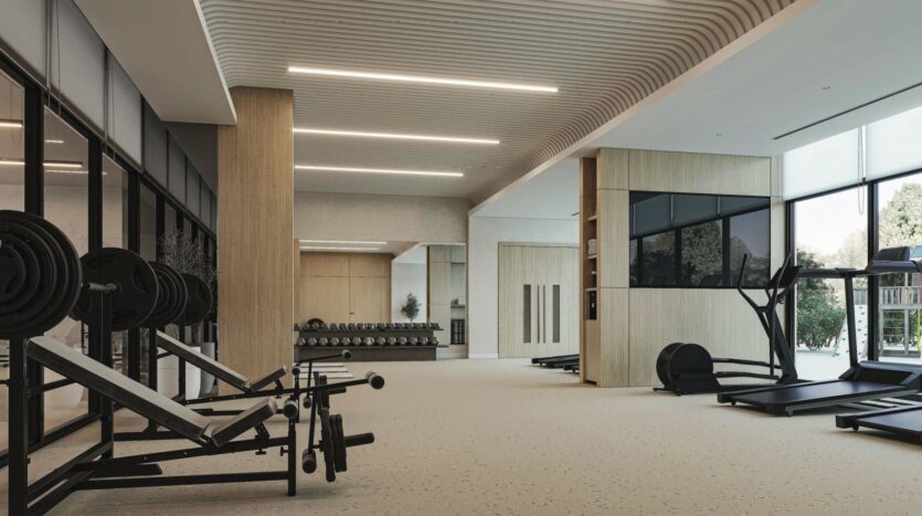 Salle de sport spacieuse et moderne à Vida Residences Saadiyat Island avec des bancs de musculation, des haltères, des tapis de course, de grandes fenêtres, des tons neutres et des plafonniers élégants. La salle bien éclairée est équipée d'appareils de fitness bien rangés.