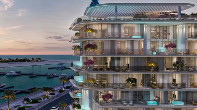 La Villa Del Garda, un immeuble d'appartements moderne situé au bord de l'eau, dispose de grands balcons en verre et de plantes luxuriantes, donnant sur un port de plaisance avec des bateaux à quai et des palmiers bordant la rue au coucher du soleil.