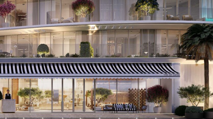 Un bâtiment moderne avec des murs en verre, un auvent rayé noir et blanc et des plantes en pot sur les balcons et à l'entrée. Une personne se tient sur un podium près de l'entrée de la Villa Del Garda, avec des palmiers visibles sur la droite.