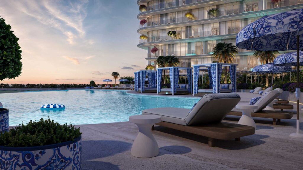 Piscine luxueuse au coucher du soleil à la Villa del Garda, avec des chaises longues rembourrées, des parasols bleus et blancs, des cabanas, des palmiers et un bâtiment moderne incurvé. La piscine tranquille reflète le ciel tandis que des plantes décoratives bordent la scène sereine.