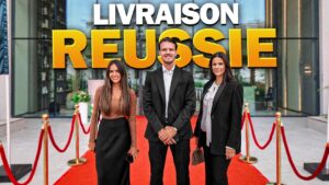 Trois personnes en tenue de travail se tiennent en souriant sur un tapis rouge devant la résidence du boulevard Avelon, à Arjan, avec des poteaux et des cordes dorés de chaque côté. Au-dessus d'eux, un grand texte indique : "LIVRAISON REUSSIE. Visite complète.
