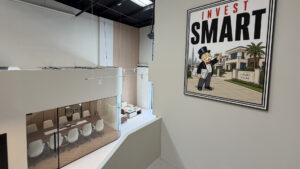 Intérieur de bureau moderne, avec en contrebas une salle de réunion aux parois vitrées et une grande affiche murale représentant la mascotte du Monopoly et portant l'inscription « Invest Smart », à côté d'une illustration de villas haut de gamme — une source d'inspiration idéale pour les investisseurs des bureaux de Dubai Immo à Dubaï.
