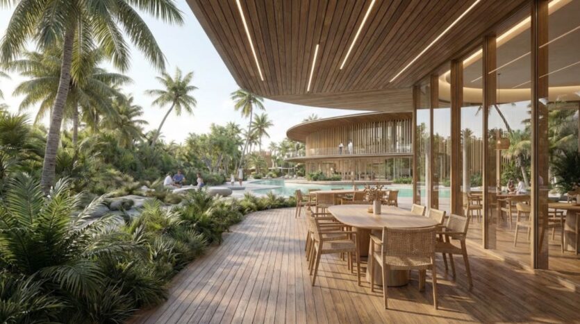 Lunaya Terraces est un complexe hôtelier tropical moderne doté d'une terrasse en bois équipée de tables et de chaises de jardin, entourée de palmiers luxuriants et d'une végétation verdoyante. De grandes baies vitrées reflètent la piscine et d'autres coins salon en arrière-plan.