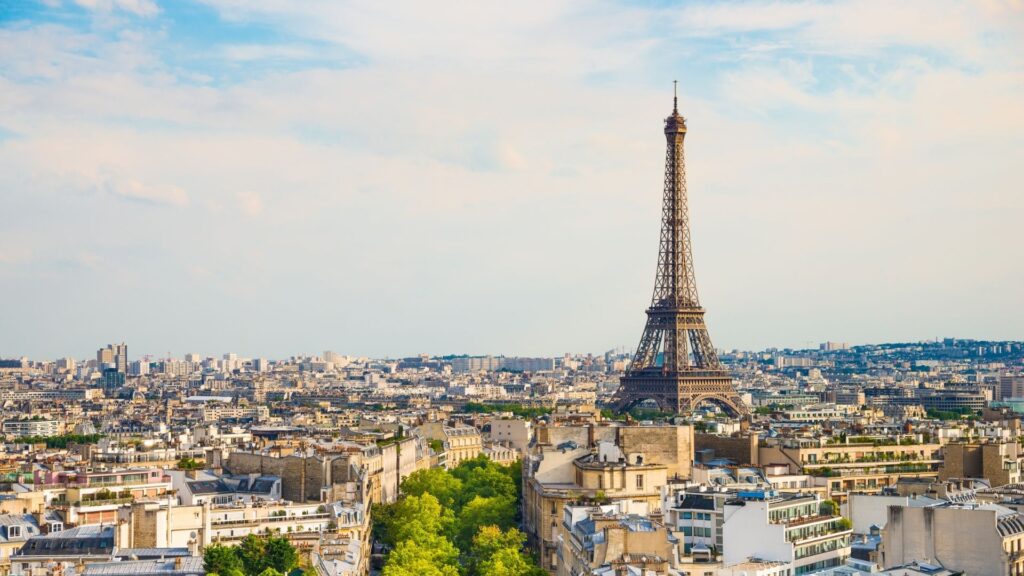 Une vue panoramique de Paris où la Tour Eiffel se détache sur les toits de la ville, avec ses bâtiments classiques et ses arbres verdoyants sous un ciel partiellement nuageux — une image qui incarne une beauté intemporelle et inspire des idées pour des projets immobiliers en 2026, de Paris à Dubaï.