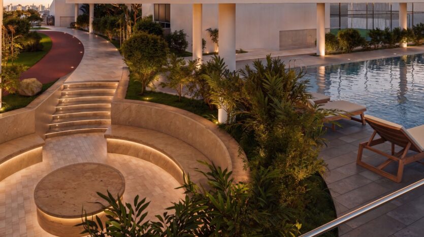 Espace extérieur moderne au crépuscule au Beverly Crown by HMB, comprenant un coin salon circulaire en contrebas, des marches éclairées, une végétation luxuriante, une piscine, des chaises longues et une piste de course jouxtant un bâtiment contemporain.