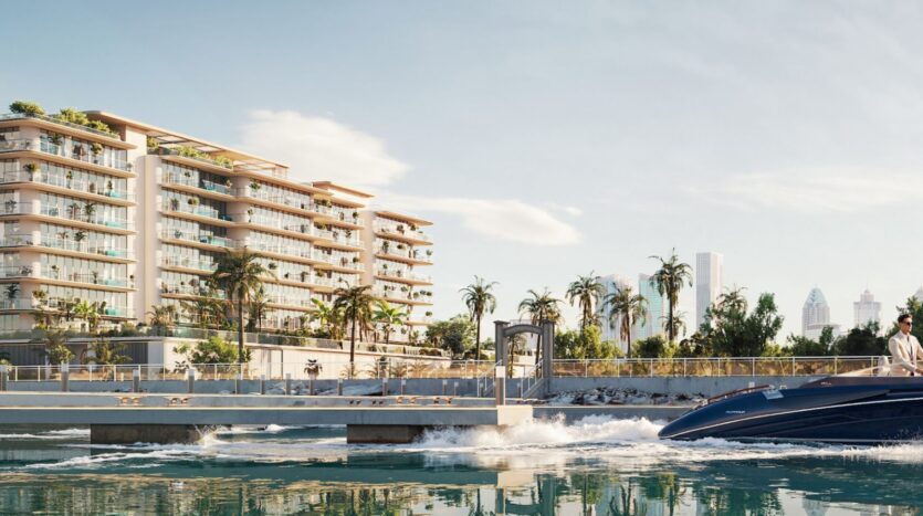 « Le Château Piétrus », un immeuble d'appartements moderne situé en bord de mer, présente des balcons donnant sur des palmiers luxuriants et quelques personnes qui profitent du panorama à l'extérieur. Au premier plan, une personne à bord d'un hors-bord file sur l'eau, tandis qu'à l'arrière-plan, les gratte-ciel de la ville se dressent sous un ciel dégagé.