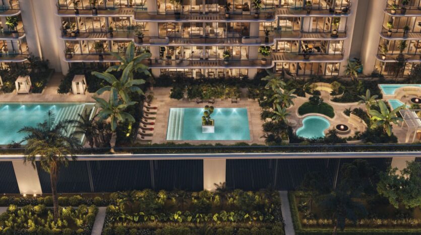 Vue aérienne, de nuit, du luxueux complexe résidentiel « Le Château Piétrus », avec ses balcons illuminés, ses piscines, ses chaises longues, ses palmiers et ses jardins paysagers.