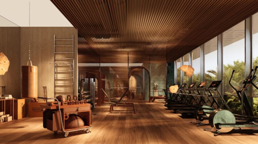 Une salle de sport spacieuse dotée d'un parquet, avec des tapis de course installés près de grandes baies vitrées, des appareils de musculation, un sac de frappe, des kettlebells et une échelle. La lumière naturelle inonde la pièce, créant une atmosphère chaleureuse et accueillante qui rappelle celle du Château Piétrus.