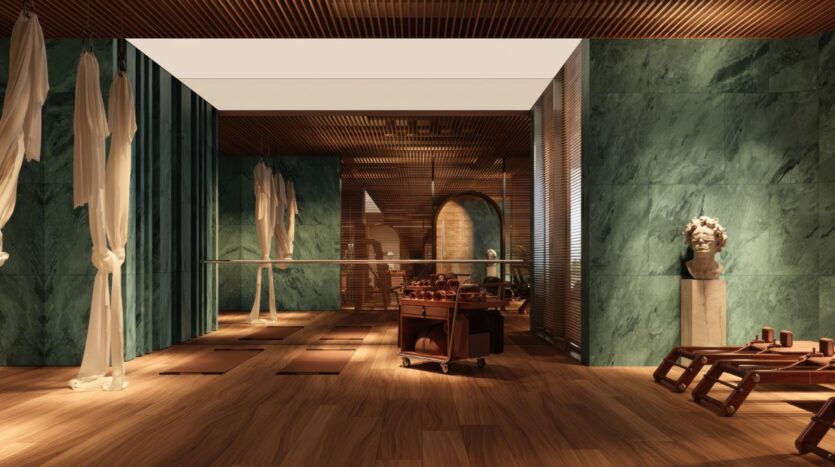 Une chambre luxueuse du Château Piétrus est dotée de murs en marbre vert, d'un parquet, de tapis de yoga, de miroirs, de tissus drapés, d'un chariot à roulettes contenant des serviettes et d'un buste classique posé sur un piédestal. Un éclairage chaleureux crée une atmosphère calme et élégante.