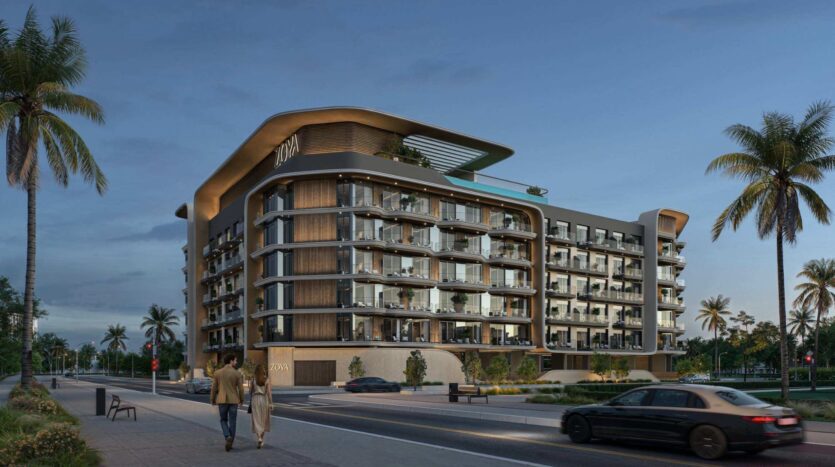 Cet immeuble d'appartements moderne à plusieurs étages, doté de balcons vitrés et entouré de palmiers, évoque le charme raffiné de « Mirari Lagoon » de Zoya. Un couple se promène sur le trottoir, tandis qu'une voiture passe dans la rue au premier plan, sous la lumière du début de soirée.