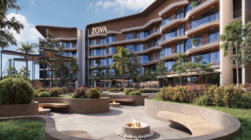 Hôtel moderne doté de balcons incurvés, baptisé « ZOYA ». Surplombant la paisible lagune Mirari by Zoya, la cour paysagée est agrémentée de bancs circulaires, d’une végétation luxuriante, de foyers et de palmiers, créant ainsi un espace extérieur propice à la détente sous un ciel partiellement nuageux.