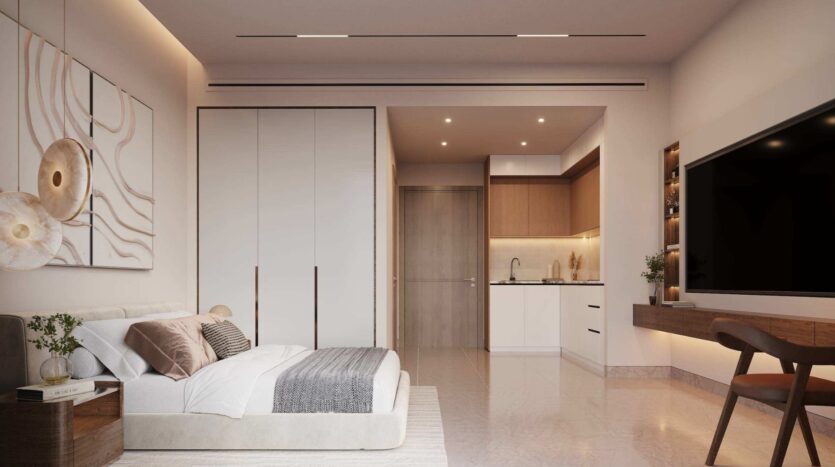 Studio moderne comprenant un lit, une décoration murale inspirée de la lagune de Mirari signée Zoya, une petite kitchenette, une armoire encastrée, une télévision fixée au mur, un bureau, une chaise et une décoration aux tons neutres. L'éclairage chaleureux et le mobilier minimaliste créent une ambiance douillette et accueillante.