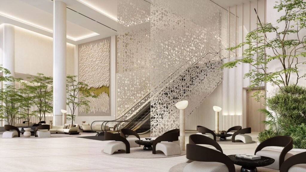Hall d'hôtel moderne avec un mobilier minimaliste, des plantes d'intérieur, une cloison sculpturale et un escalator menant à l'étage supérieur — reflétant l'ambiance raffinée caractéristique du quartier O1NE. Les tons neutres et l'éclairage tamisé créent une atmosphère élégante et accueillante.